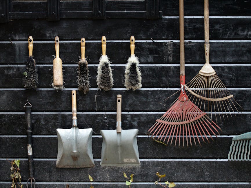 A close-up view of a person wearing a light-colored glove and a wristwatch, using a shovel to place a mixture of garden debris, including small twigs, leaves, and bits of concrete or gravel, into a la